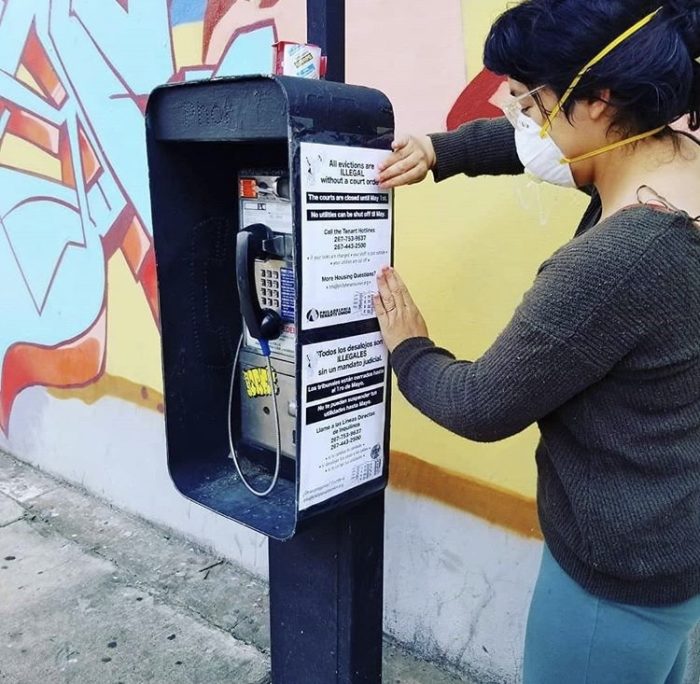 A Philadelphia Tenants Union member attaching a poster to a telephone box. The sign reads "all evictions are illegal".